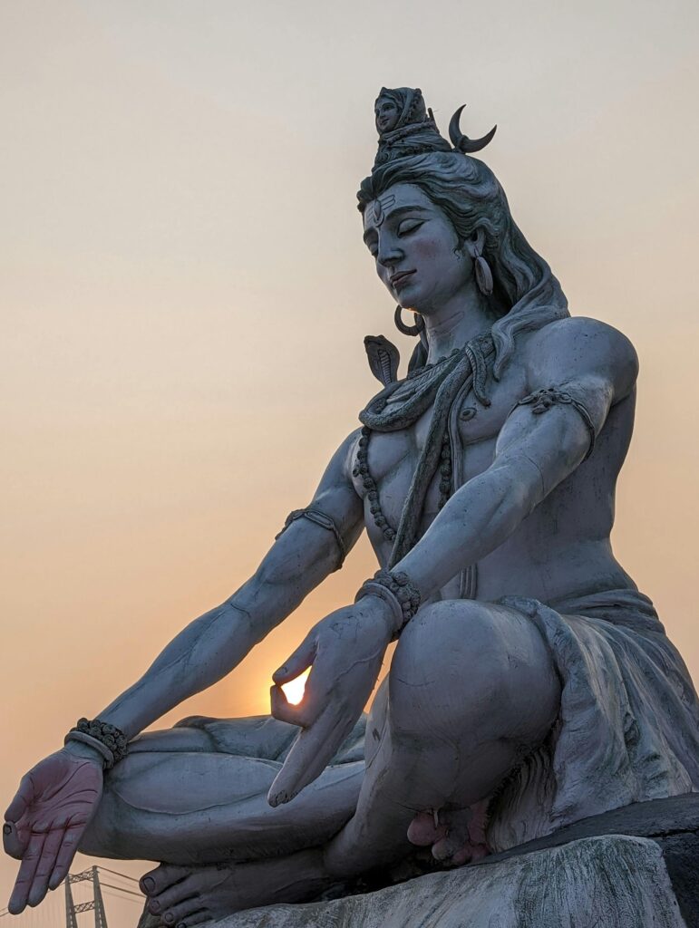 A majestic statue of Lord Shiva in a meditation pose during a tranquil sunset.